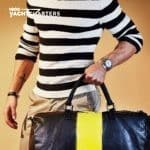 Person in horizontal blue and white striped shirt. He is holding a duffle bag. The bag is navy blue with a yellow vertical stripe.
