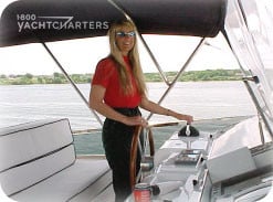 Photograph of Jana Sheeder behind the steering wheel of a motoryacht at anchor. She is wearing black pants and red shirt.