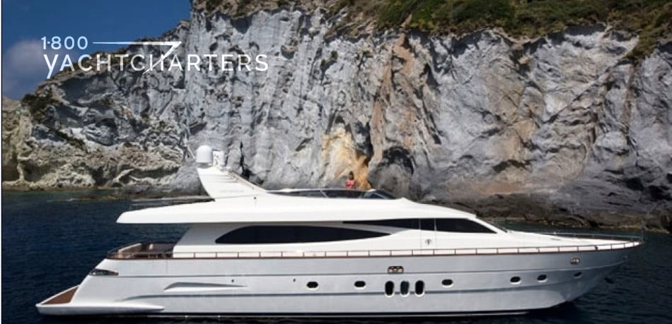 Profile photograph of motoryacht VALENTINA, facing the right side of the picture.  There is a large cliff behind her.  She is at anchor.