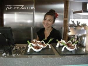 yacht charter chef caro uy poses in the galley of a yacht. On the counter in front of her are 4 rippled white plates of textured items, unknown what they are