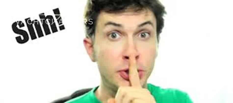 Photograph of a man in a green shirt with his finger to his lip, indicating for you to be quiet.  It says Shh! in black bold font on the left side of his head.