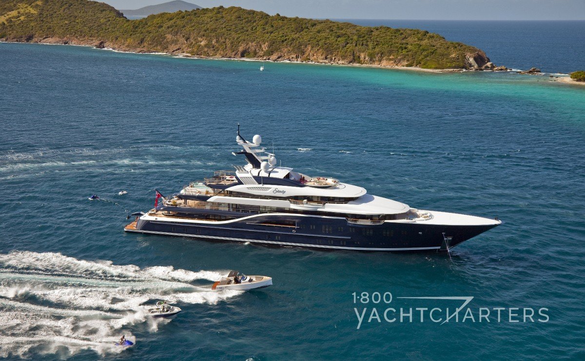 Blue-hulled superyacht with white superstructure anchored next to an island - watertoys in water and running