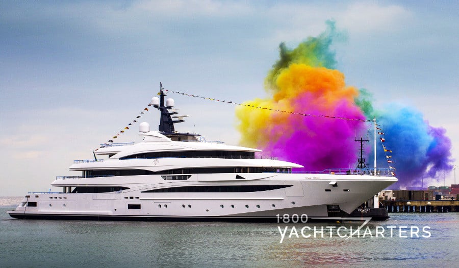 ODYSSEY launch with green orange and pink smoke in the background of the bow and colorful banner flags across length of yacht