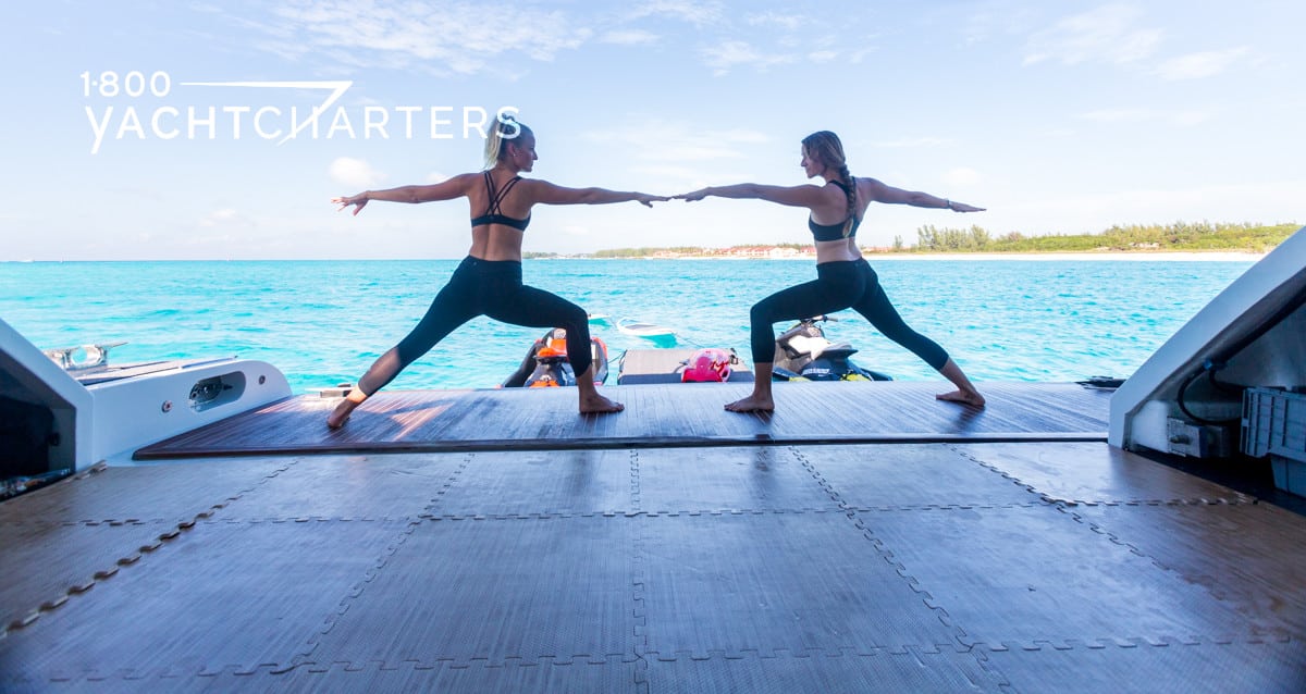 Two women doing yoga Warrior One on the beach club aft deck swim platfform