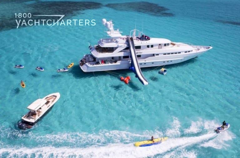 luxury yacht charter boat at anchor with inflatable slide from top deck to water, and guests on watertoys surrounding the yacht