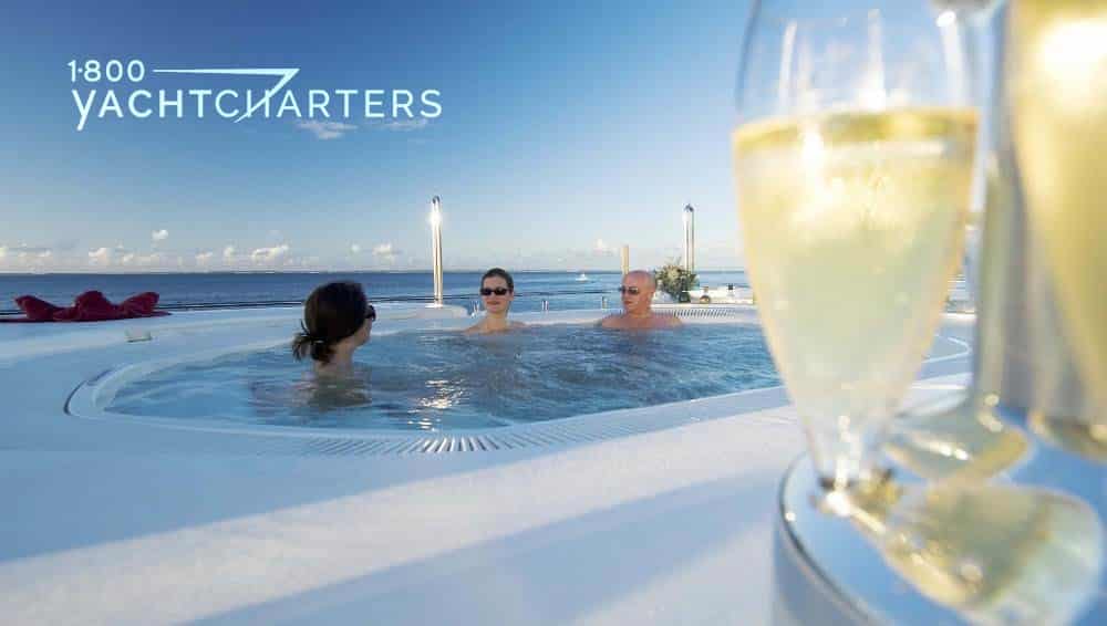 three people sitting in a spa on the deck of a yacht - full champagne glasses in foreground of photo