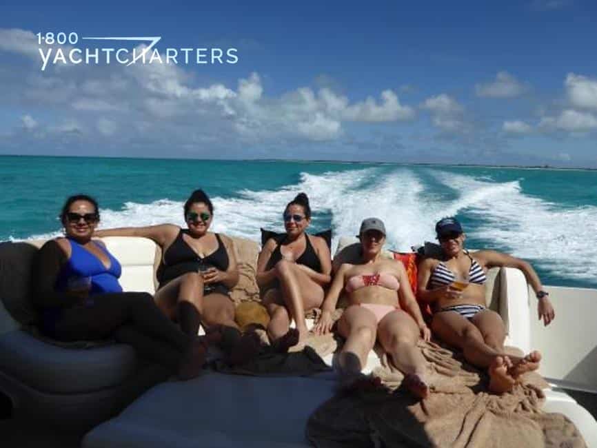Five girls relaxing in sun lounges at the back of a speeding boat