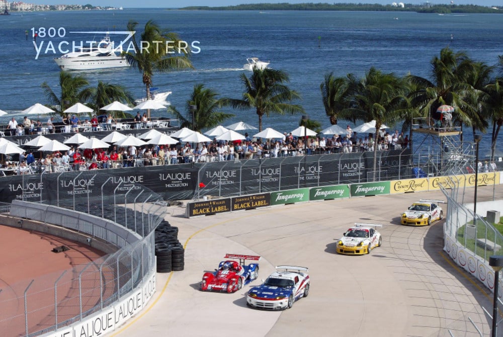 Four race cars on a winding street beside the ocean. Lalique and Black Label banners behind the cars as they whiz by.