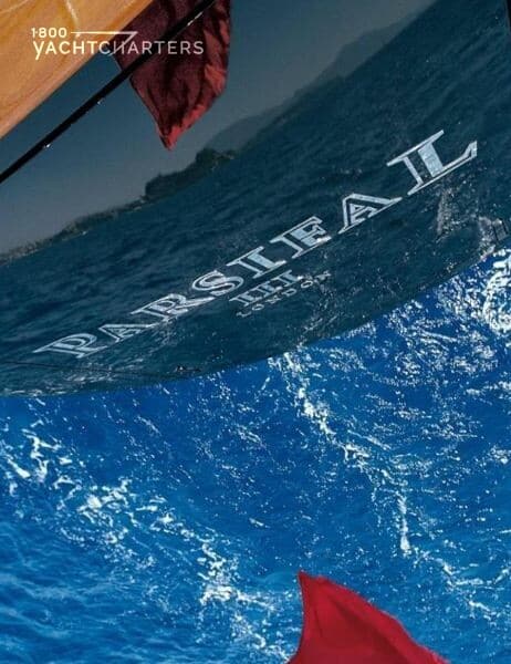 Photograph of the back of the sailboat underway. The photo shows part of the name of the sailboat. It says PARSIFAL. The waves are lapping at the bottom of the sailboat as it seemingly sails along. Yacht is featured on bravo television series, Below Deck