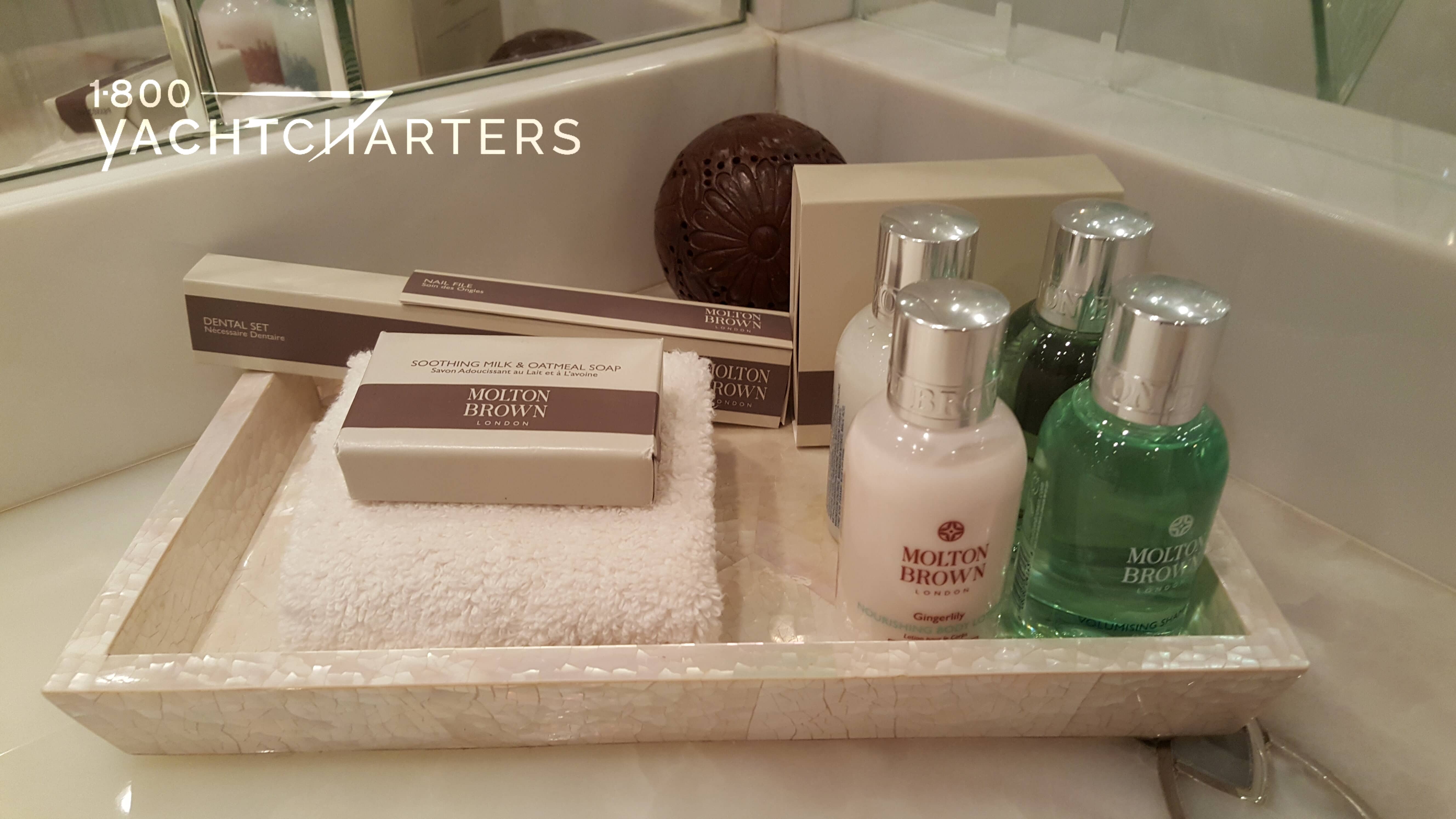 Photograph of a tray of bath products on a yacht. The products are all made by Molton Brown. The tray is beige, and the vanity is light colored marble.